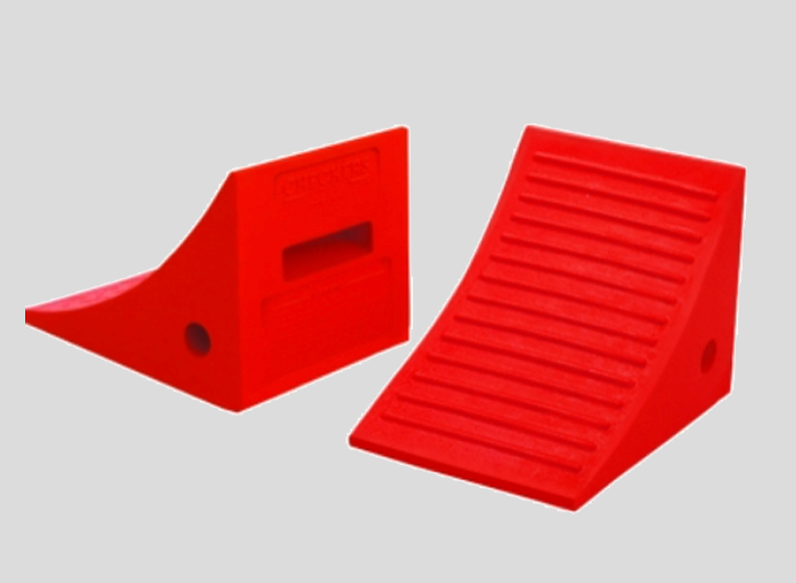 Two red plastic ramps on a gray background, used as wheel chocks or dock bumpers.