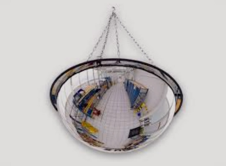 A convex traffic mirror hanging from a chain on a wall.