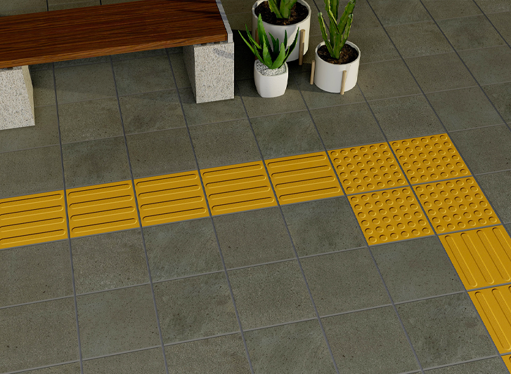A bench is sitting on a tiled floor next to a potted plant. The tiles incorporate stainless steel studs for increased durability and the prevention of wear and tear.