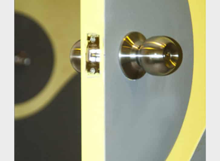 A close up of a yellow door with a metal handle, featuring PVC wall guards on the surrounding walls.