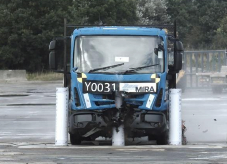 A blue truck is driving down a road, passing by stainless steel bollards.