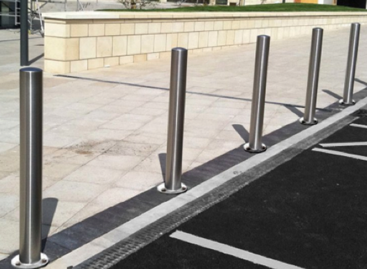 A group of stainless steel bollards in a parking lot.