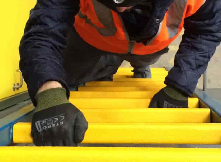 A man wearing a safety vest and gloves on a yellow stair with aluminium stair nosing.