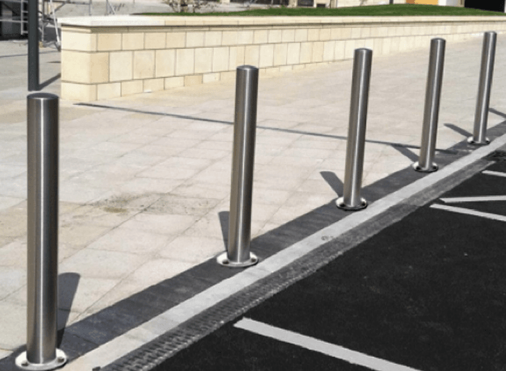 A group of stainless steel bollards in a parking lot.